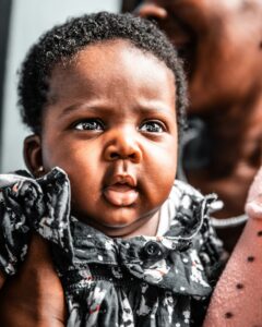 Adorable African American baby in dress looks on.